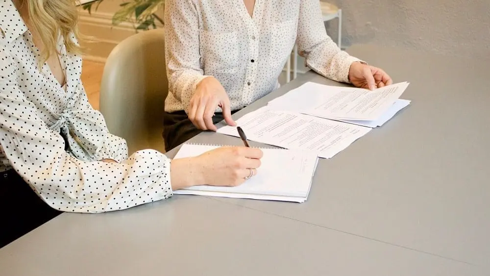 Dos personas sentadas en un escritorio hablando sobre documentos.